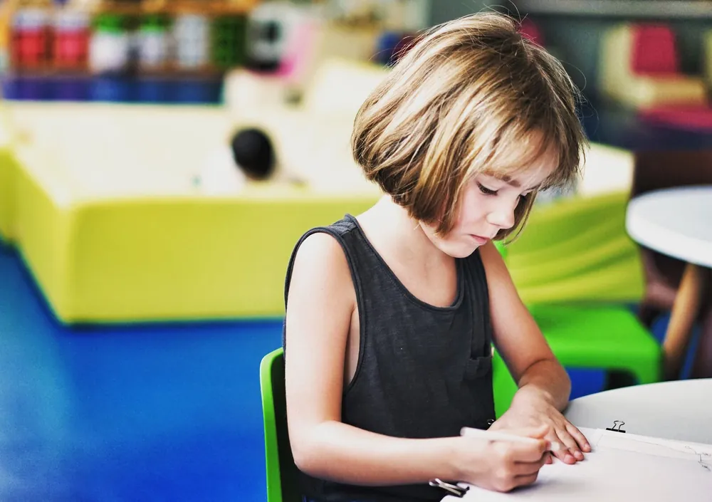 A girl sat at a table writing on a piece of paper